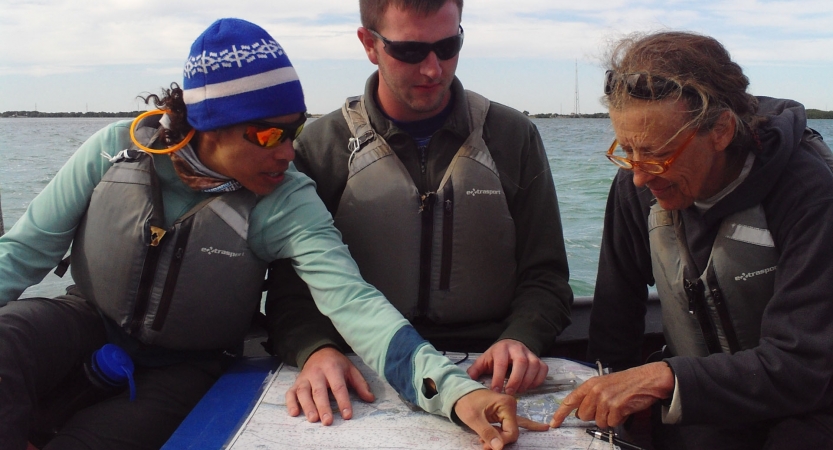 Three people wearing life jackets sit on a boat examining a map.